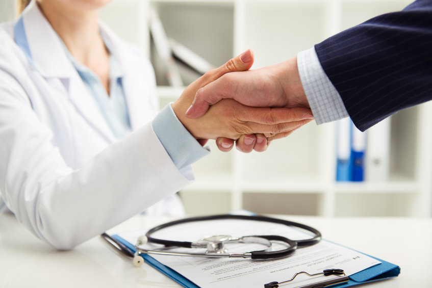 Woman doctor shaking hand with businessman in the office. Young medical specialist in uniform meeting partner for discussion. Shallow depth of field.